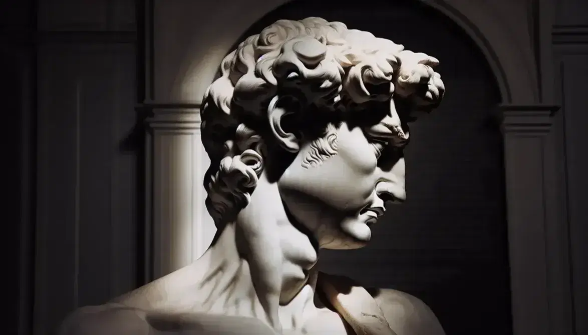 Testa e spalla destra della statua del David di Michelangelo in marmo bianco, con dettagli del viso illuminati e sfondo sfocato.