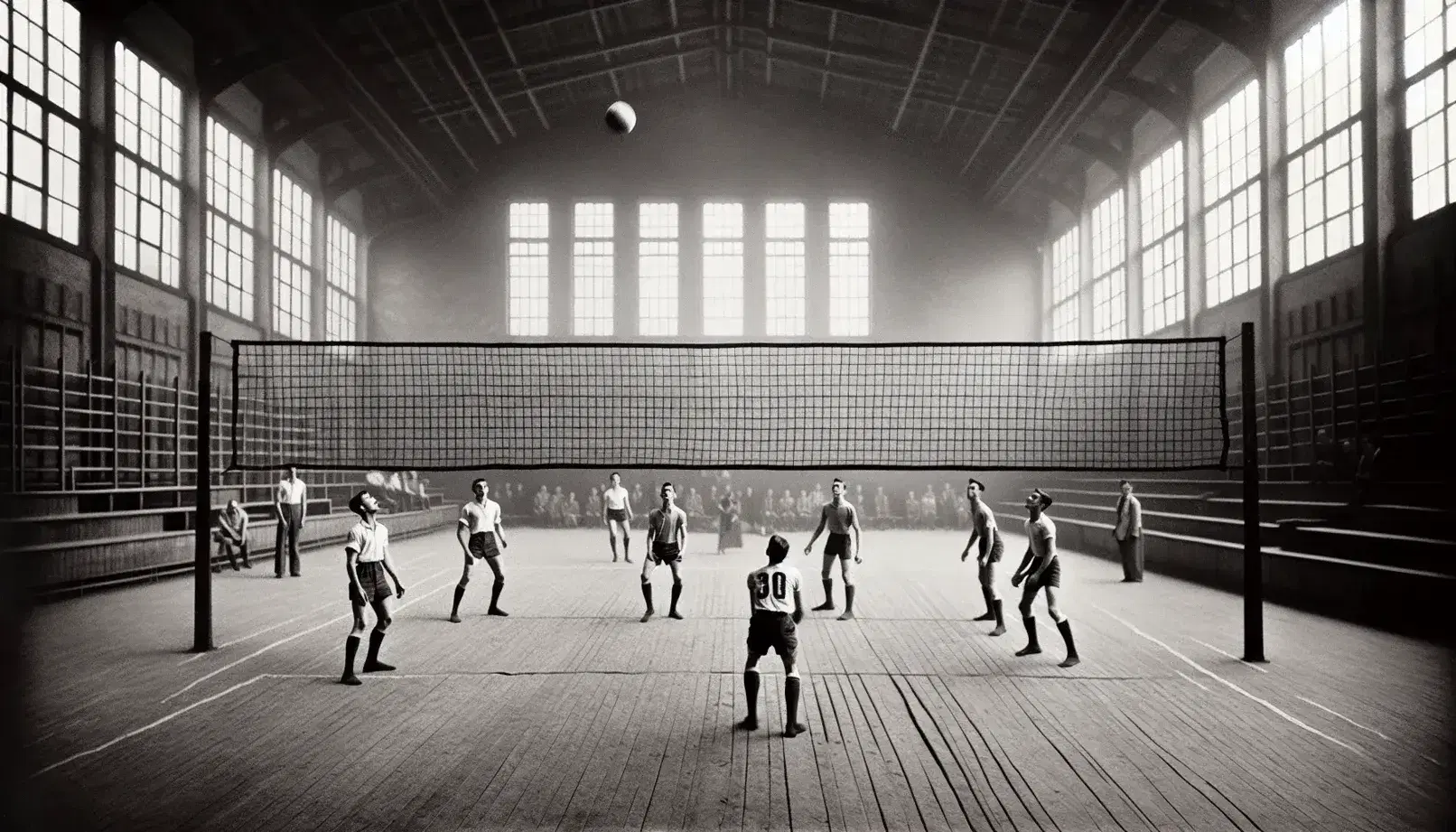 Grupo de personas jugando vóleibol en gimnasio antiguo, con red central y balón en movimiento sobre ella, en fotografía en blanco y negro.
