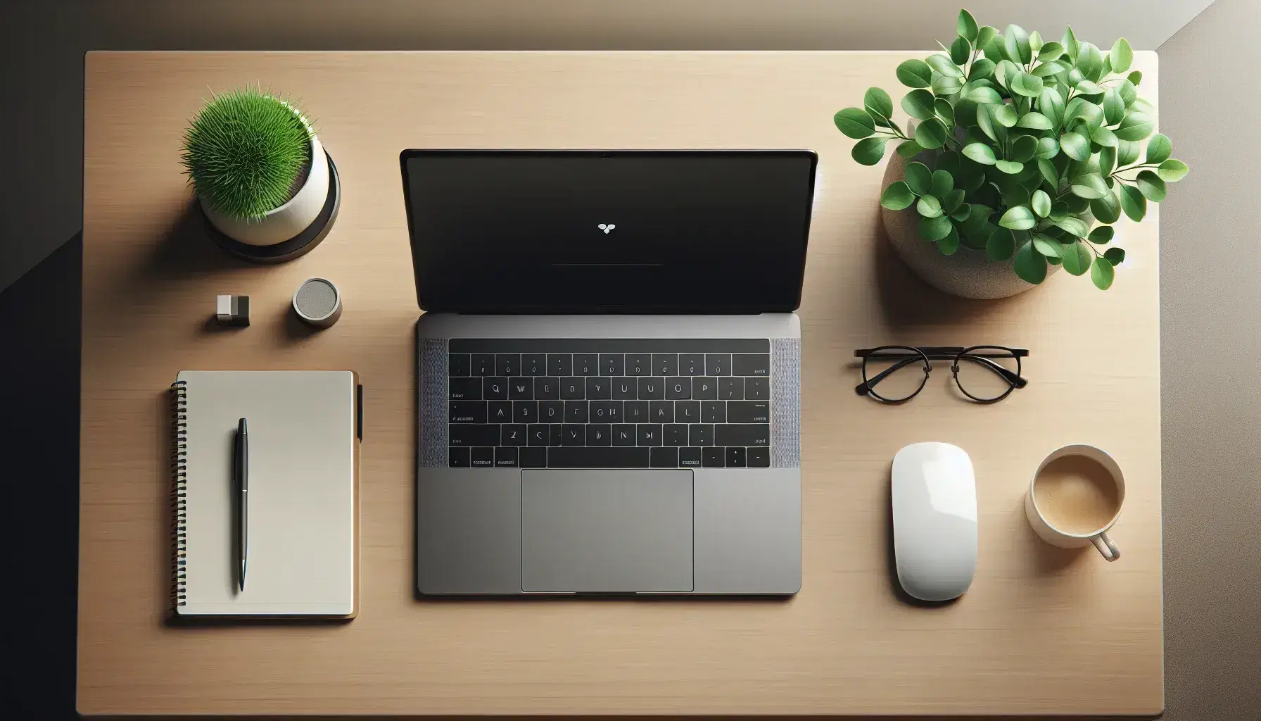 Tidy desk with open laptop, black wireless mouse, notebook, coffee cup and green plant, glasses in foreground.